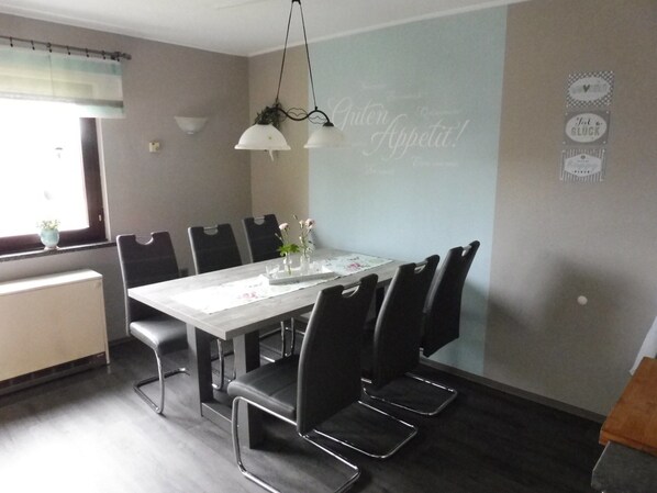 A dining area with a long table, black chairs, and hanging pendant lights.