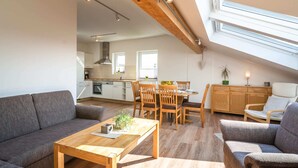 A spacious living area with a high ceiling, wooden beams, a dining table with chairs, and a kitchen in the background. - Eifel Lakeside Family Escape (Ellscheid)