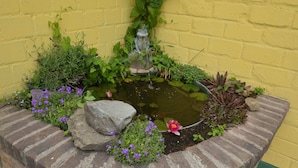 A small garden pond with a frog statue, surrounded by various plants and flowers. - Farmstay Comfort in Juchen (Juechen)