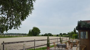 An outdoor seating area with tables and chairs, a fenced riding arena, and a small building with a window. - Farmstay Comfort in Juchen (Juechen)