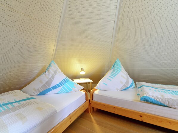 A room with two wooden beds, each with a white mattress and blue and white patterned pillows. There is a small table with a lamp between the beds. - Quaint Apartment in Eimelrod near Lake & Water Sports (Willingen)
