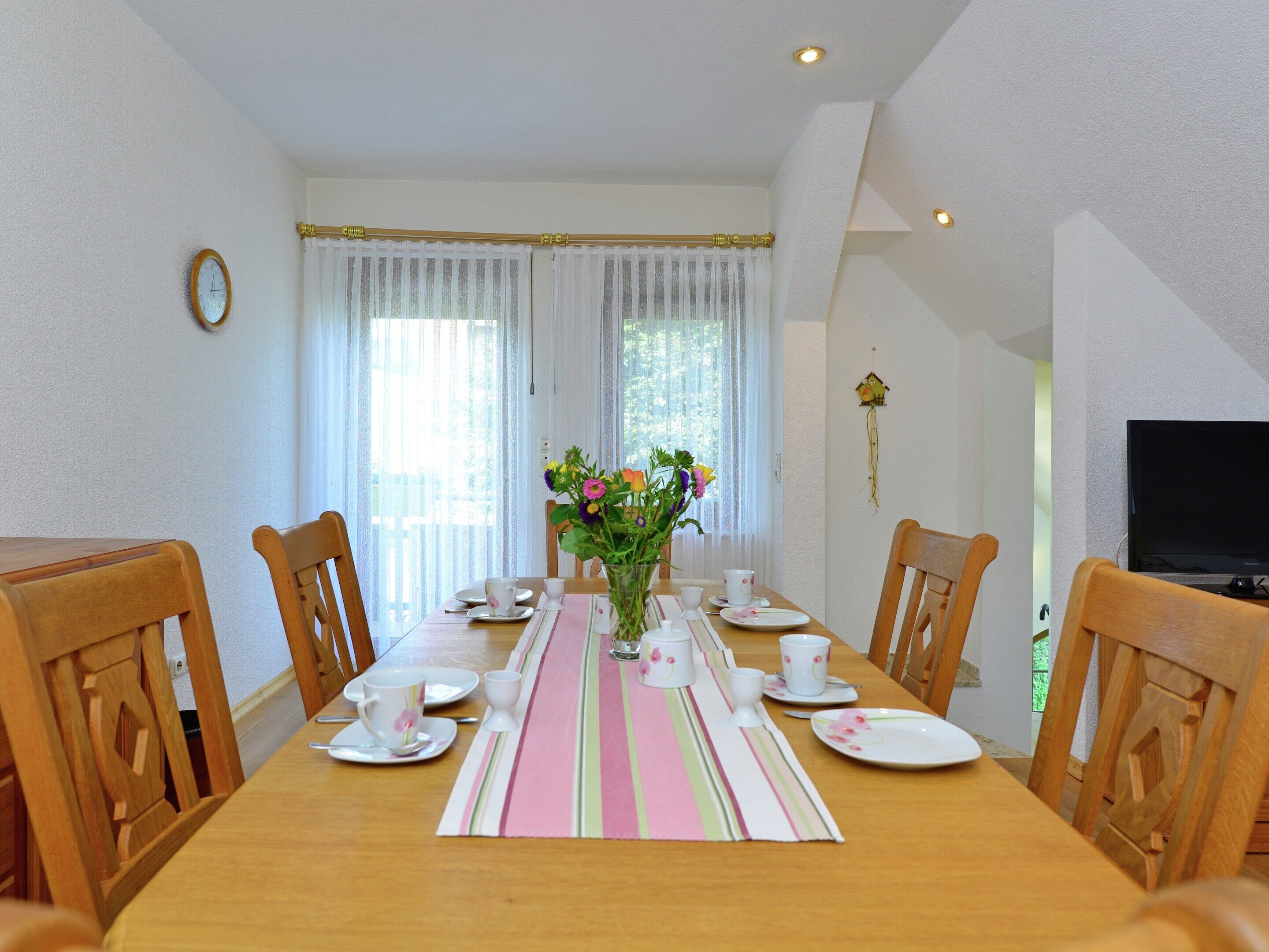 Comedor con mesa de madera dispuesta para cuatro, platos blancos, tazas y un mantel a rayas.
