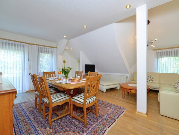 A dining area with a wooden table, chairs, and a patterned rug. There is a sofa and a small table in the background. - Quaint Apartment in Eimelrod near Lake & Water Sports (Willingen)