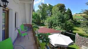 A balcony with green chairs, a white umbrella, and a view of a green landscape. - Quaint Apartment in Eimelrod near Lake & Water Sports (Willingen)