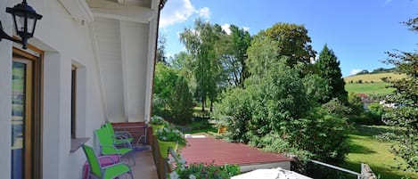 A balcony with green chairs, a white umbrella, and a view of a green landscape.