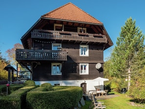 Een meerlaags houten huis met een balkon, een schotelantenne en een verzorgde tuin.