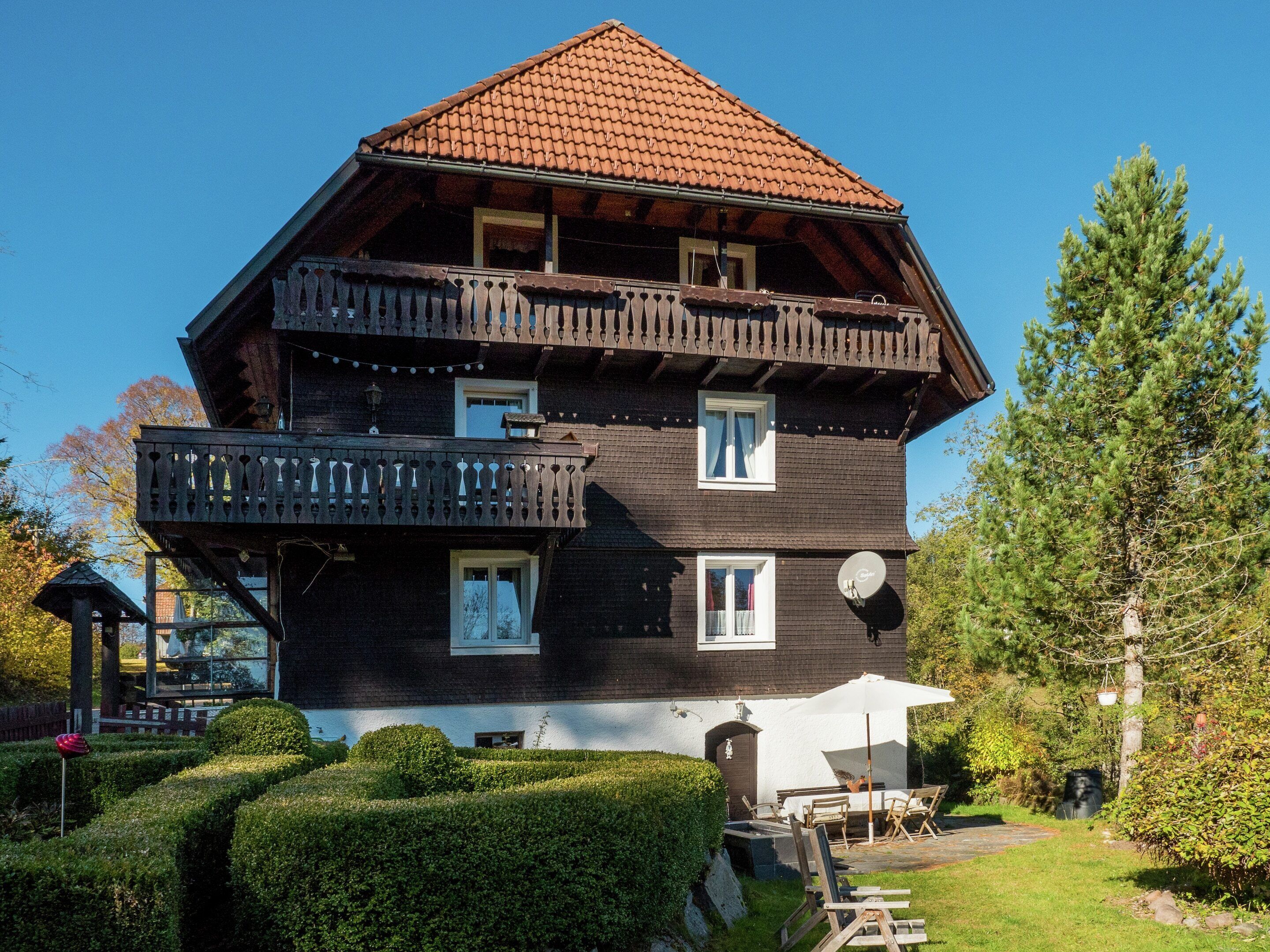 Ein mehrstöckiges Holzhaus mit Balkon, Satellitenschüssel und gepflegtem Garten.