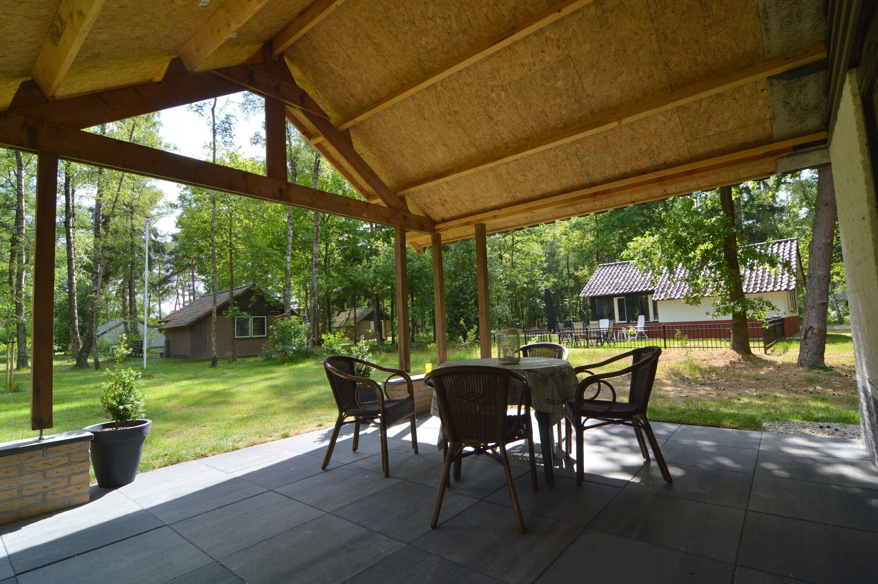 An outdoor patio with a covered seating area, surrounded by a lush green landscape and trees.