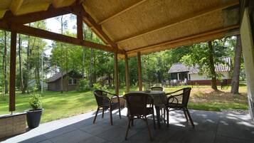 An outdoor patio with a covered seating area, surrounded by a lush green landscape and trees.