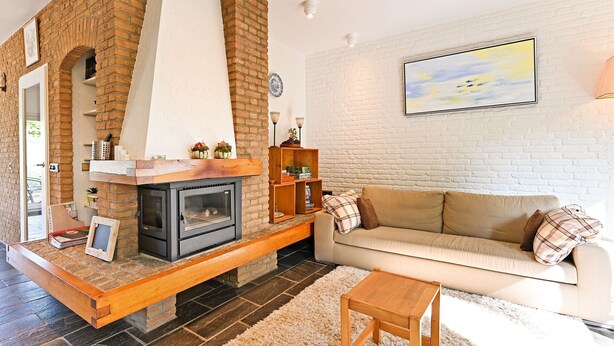 Ein Wohnzimmer mit Kamin, einer Couch, einem Couchtisch und einer weißen Ziegelwand mit einem Gemälde.