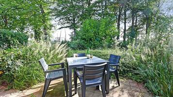 Un patio al aire libre con una mesa y sillas, rodeado de abundante vegetación y árboles.