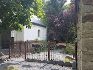 A white building with a sloped roof, surrounded by a gravel driveway and a wrought iron fence.