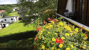 A balcony with a view of a garden and a pond, a railing, and a building in the background. - Forest Hideaway for 2 Guesst (Kirchhundem)