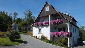 A two-story house with a sloped roof, a small balcony with flower boxes, and a paved driveway. - Forest Hideaway for 2 Guesst (Kirchhundem)