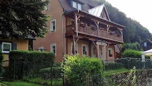 A two-story house with a balcony, surrounded by greenery and a stone wall. - Forest Hideaway for 2 Guesst (Kirchhundem)