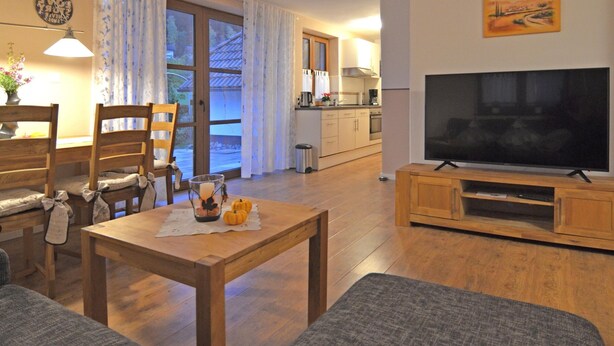 A living room with a TV, wooden furniture, a dining table with pumpkins, and a kitchen in the background. - Forest Hideaway for 2 Guesst (Kirchhundem)