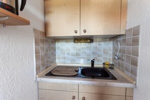 Compact kitchen area with a light-colored backsplash and a black sink.
