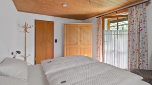 Un dormitorio con techo de madera, un armario, una cama con ropa de cama a rayas y una ventana con cortinas florales.