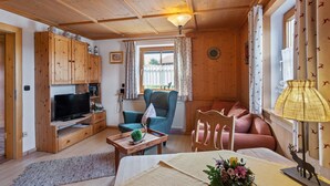 Una habitación acogedora con paredes de madera, un televisor, un sofá, una silla, una mesa con lámpara y una ventana con cortinas.
