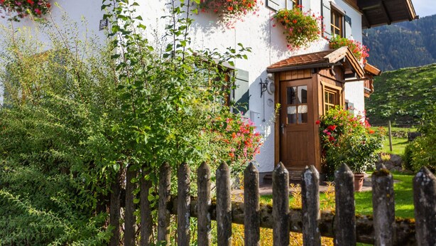 Una cabaña tradicional con puerta de madera, macetas con flores y valla de madera.
