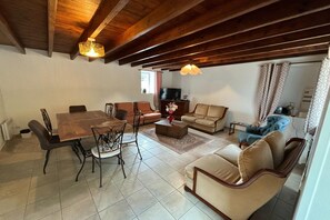 A spacious living area with a wooden dining table, sofas, and a television. - Normandy Family Escape (Ozeville)