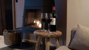 A cozy room with a fireplace, a small wooden stool, and a bottle of wine on a table. - Holiday Home in Bullange With Sauna (Buellingen)