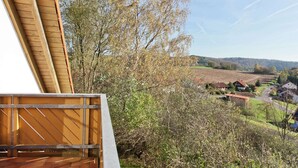 A wooden balcony with a view of a rural landscape, including fields and houses.