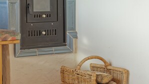 A corner of a room with a fireplace, a wicker basket with logs, and a wooden bench.