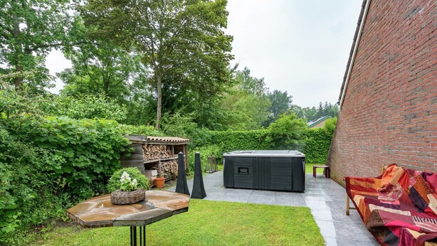 A patio area with a table, a bench, a hot tub, and a brick wall.
