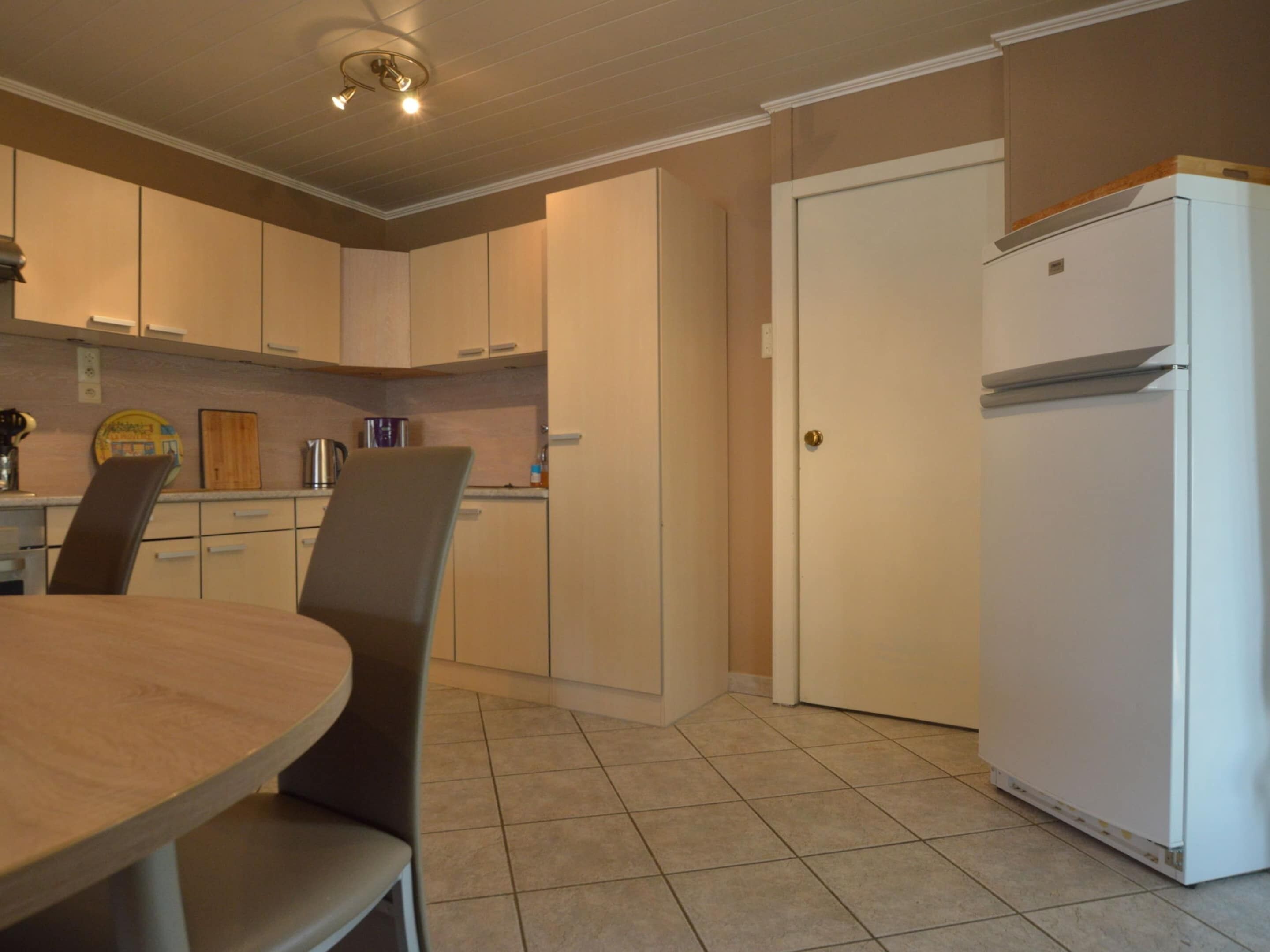 A compact kitchen with a dining table, chairs, a refrigerator, and cabinets.