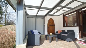 Un espacio de patio cubierto con dos sofás de mimbre, una mesita y una puerta de madera.