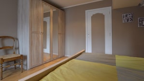 Un dormitorio con cama, armario de madera, una silla y una puerta.