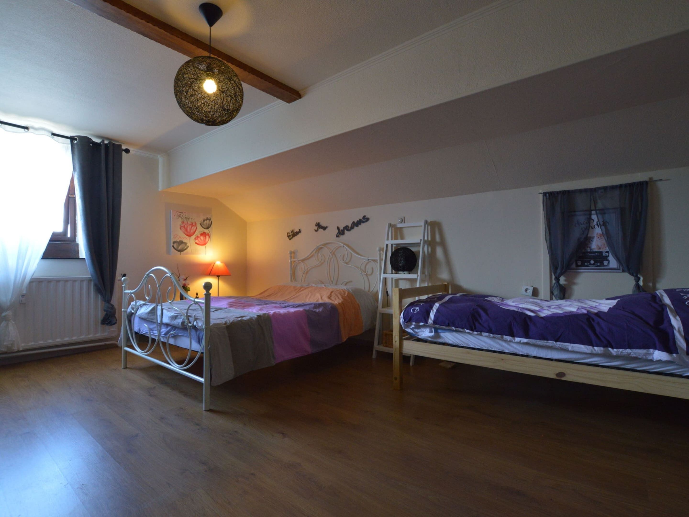A room with two beds, a ladder, a hanging light fixture, and a radiator.