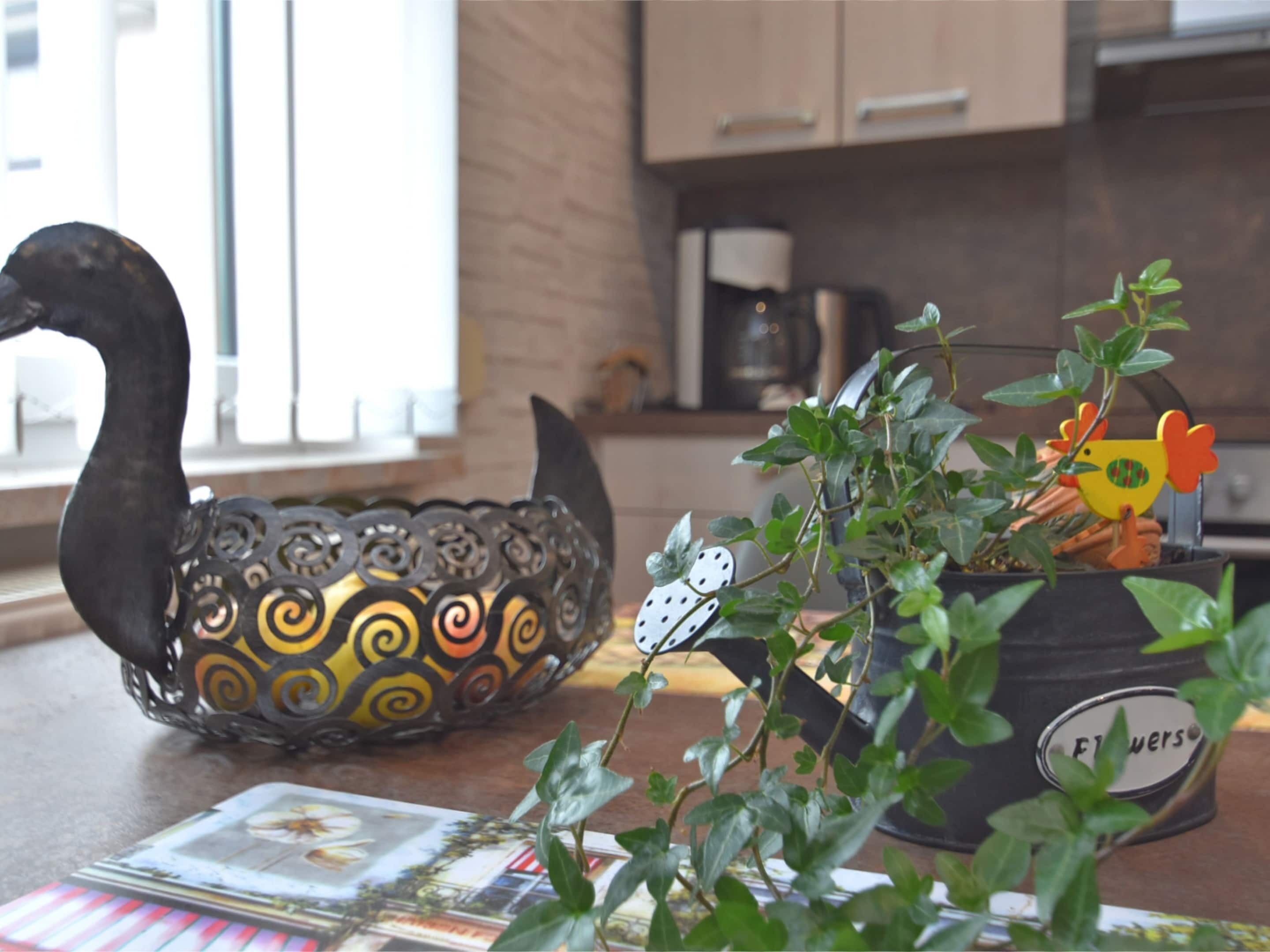 Una encimera de cocina con un cuenco decorativo con forma de cisne, una planta en maceta y un juego de cartas.
