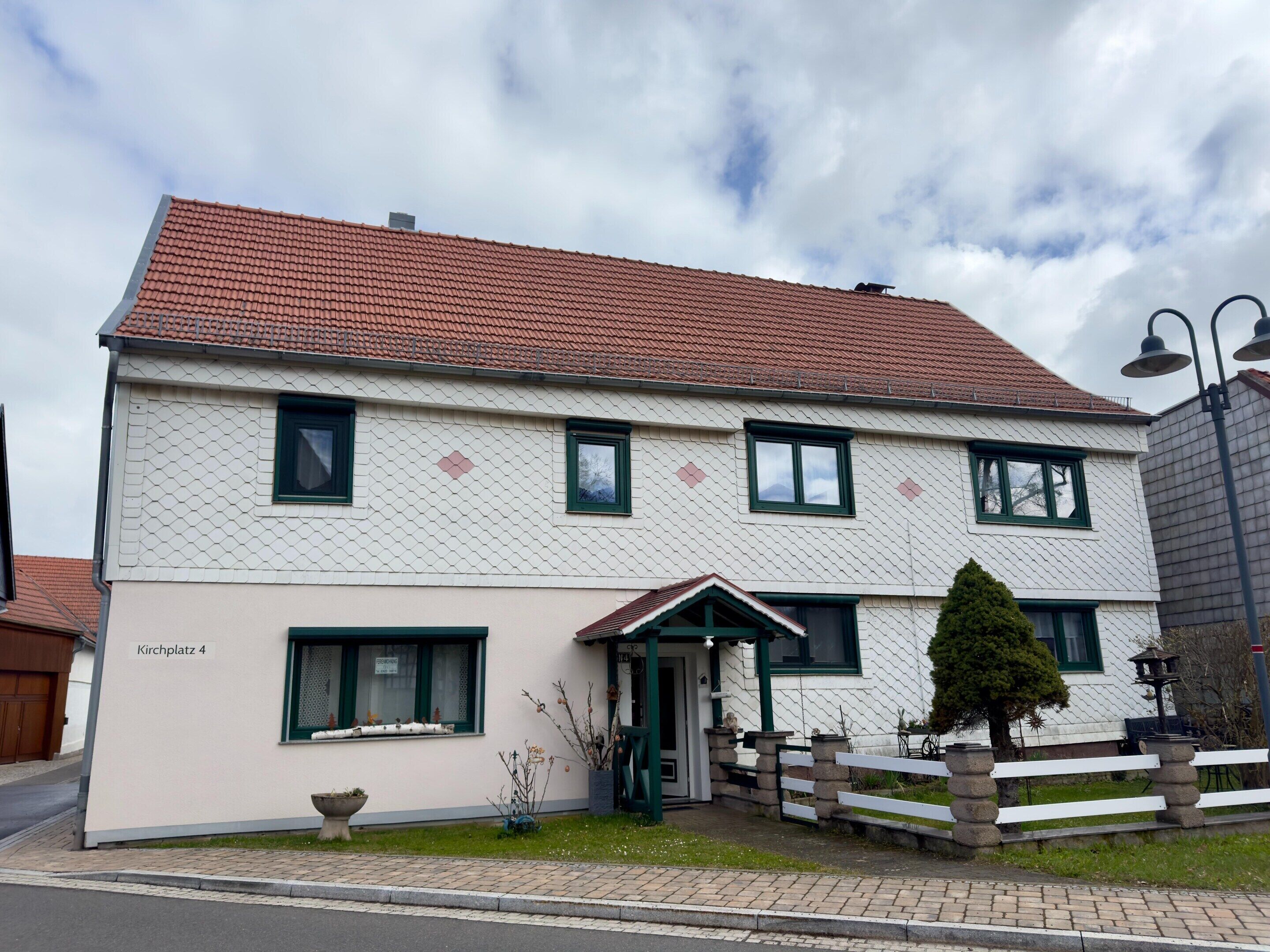 A two-story building with a tiled roof, a small porch, and a sign reading 'Kirchplatz 4'.