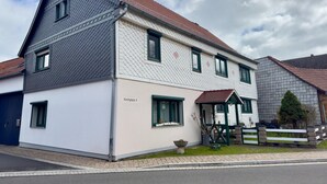 Ett tvåvåningshus med ett grått tak, vita väggar och gröna fönsterramar.