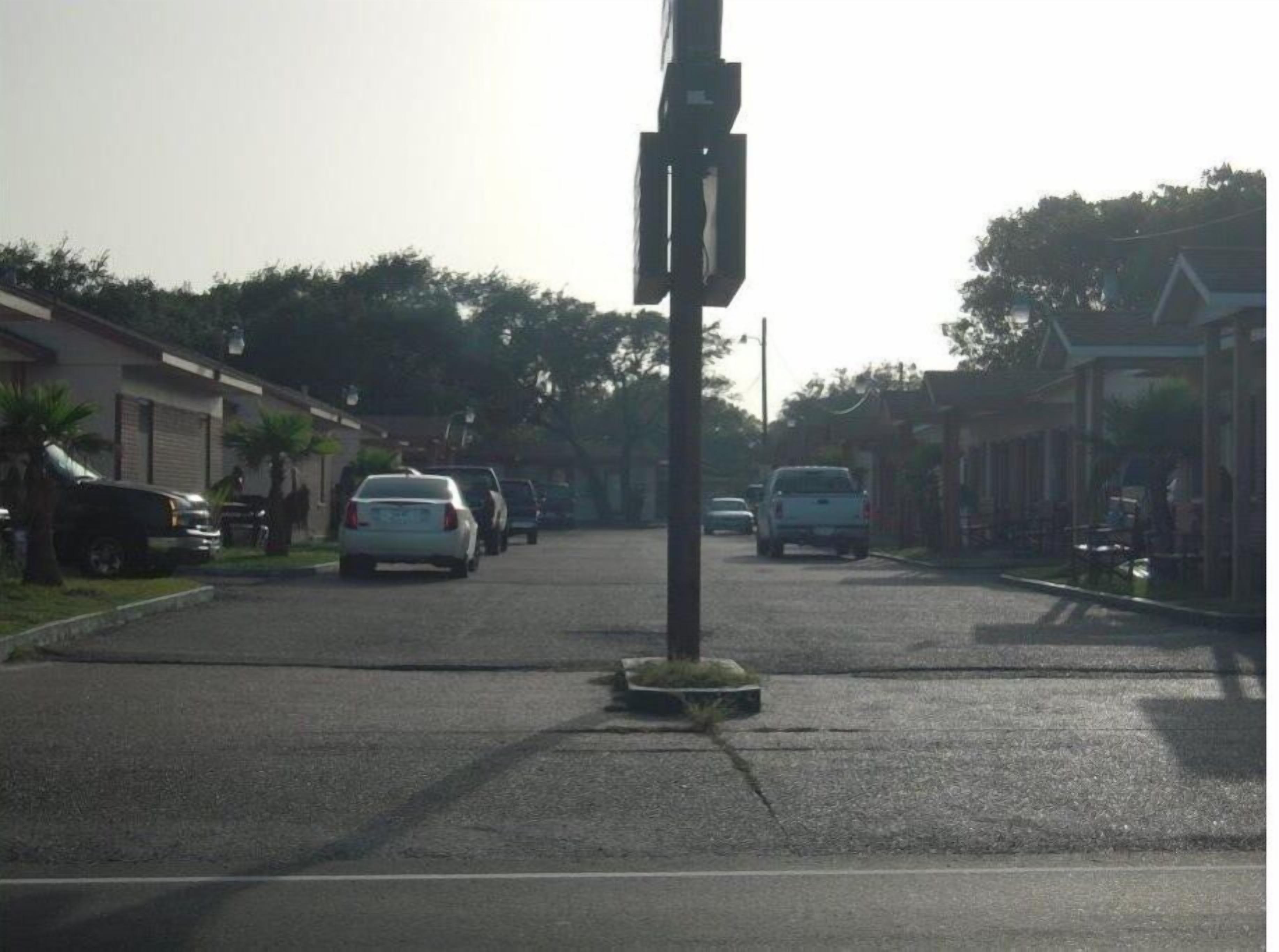 A residential street with houses on both sides, parked cars, and a traffic light in the center.