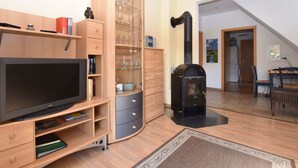 A living room with a TV, wooden cabinets, a glass display case, a black fireplace, and a dining area with a table and chairs. - Cozy Apartment in Rerik near Beach (Rerik)