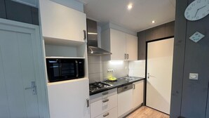 A modern kitchen with white cabinets, a black microwave, a gas stove, and a sink. - Bungalow in Limburg Near Nature Reserves (Stramproy)