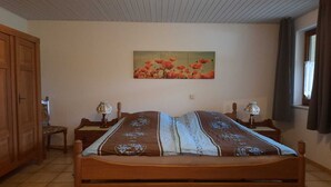 A bedroom with a wooden bed, two bedside tables with lamps, a wooden wardrobe, a painting on the wall, and a window with curtains. - Holiday Home Niederehe Romantic Escape (Üxheim)