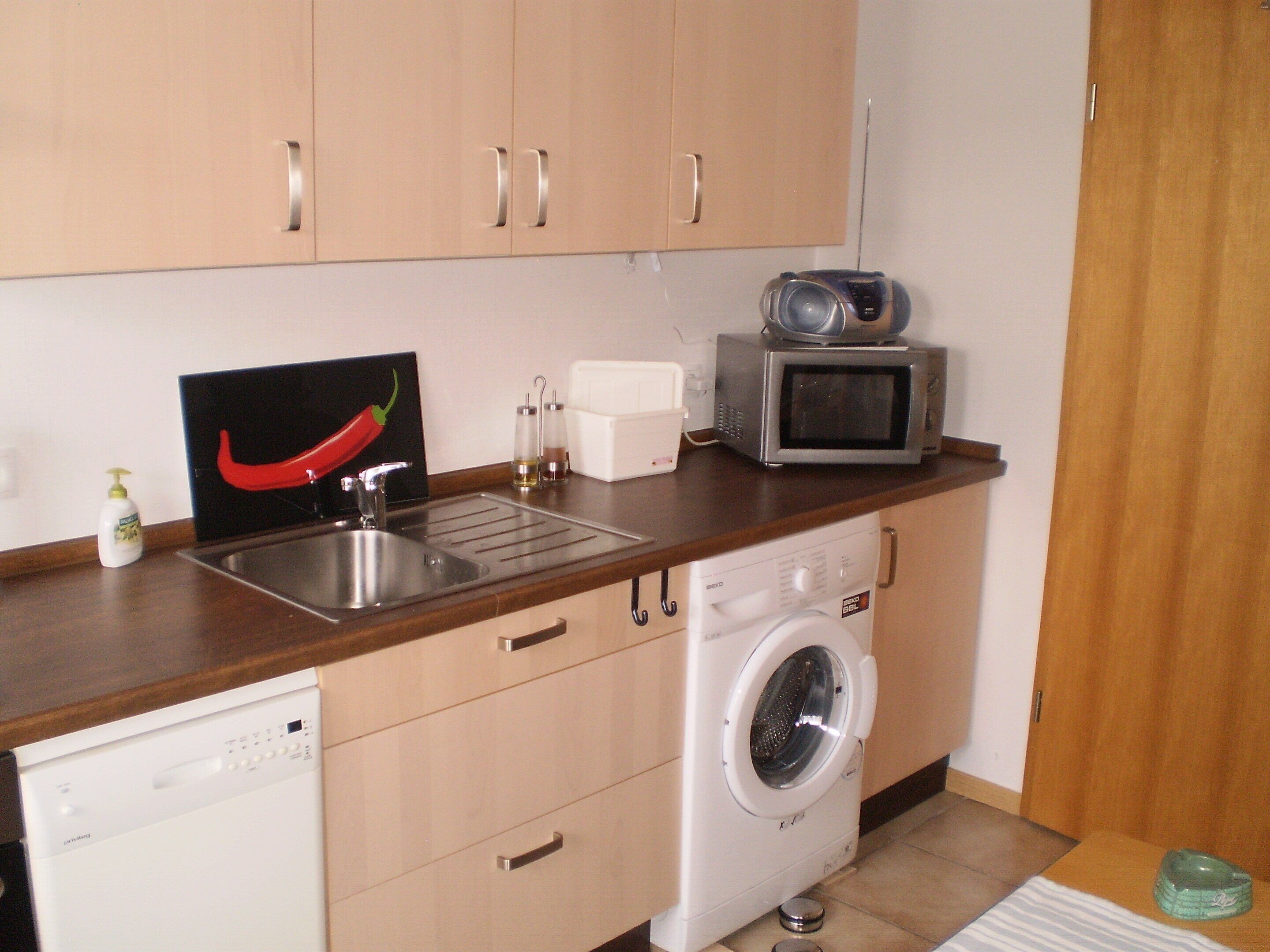 A compact kitchen with a dishwasher, washing machine, microwave, and a sink.