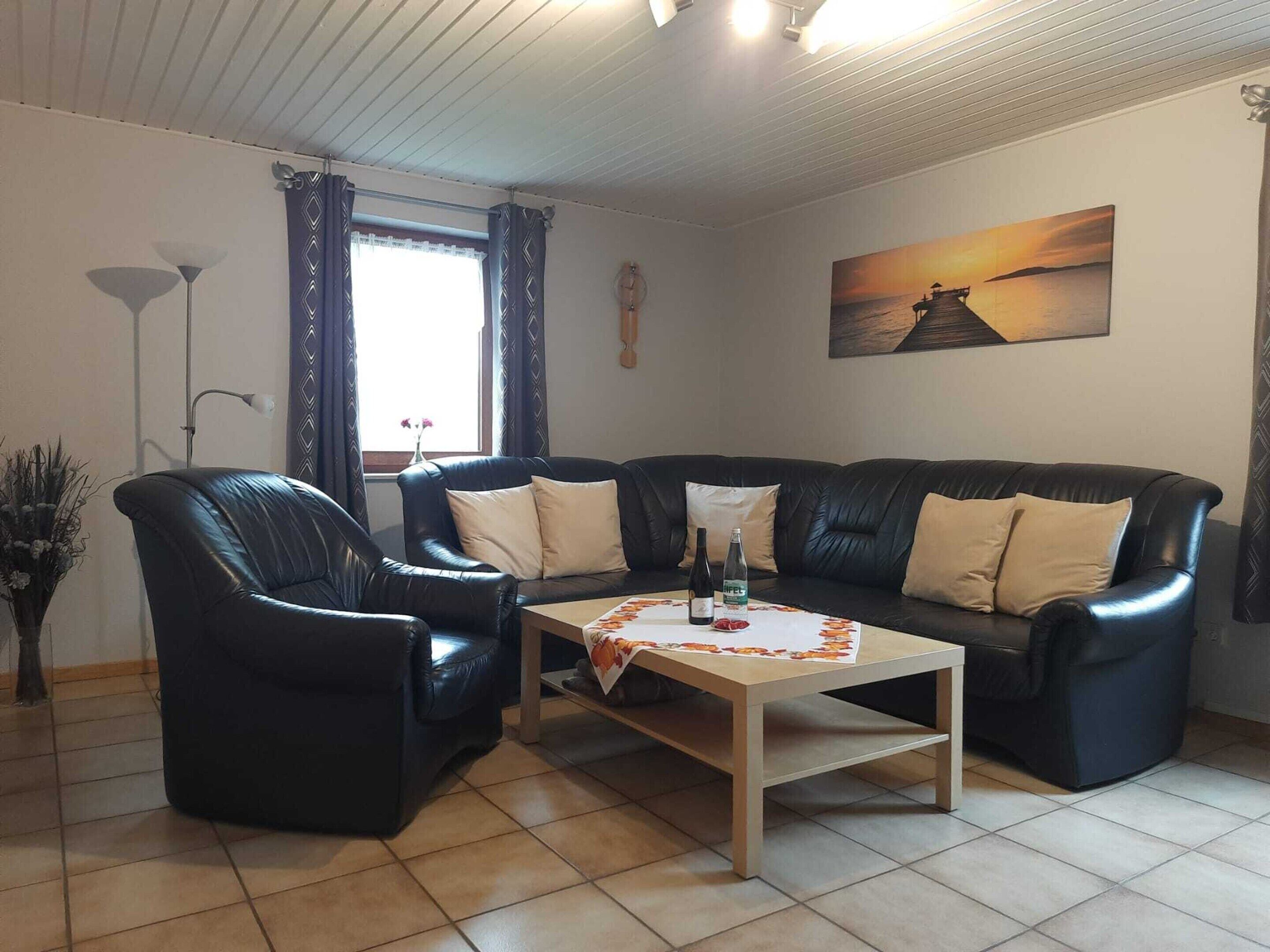 A living room with a black leather sofa, two armchairs, a wooden coffee table, and a painting of a sunset.