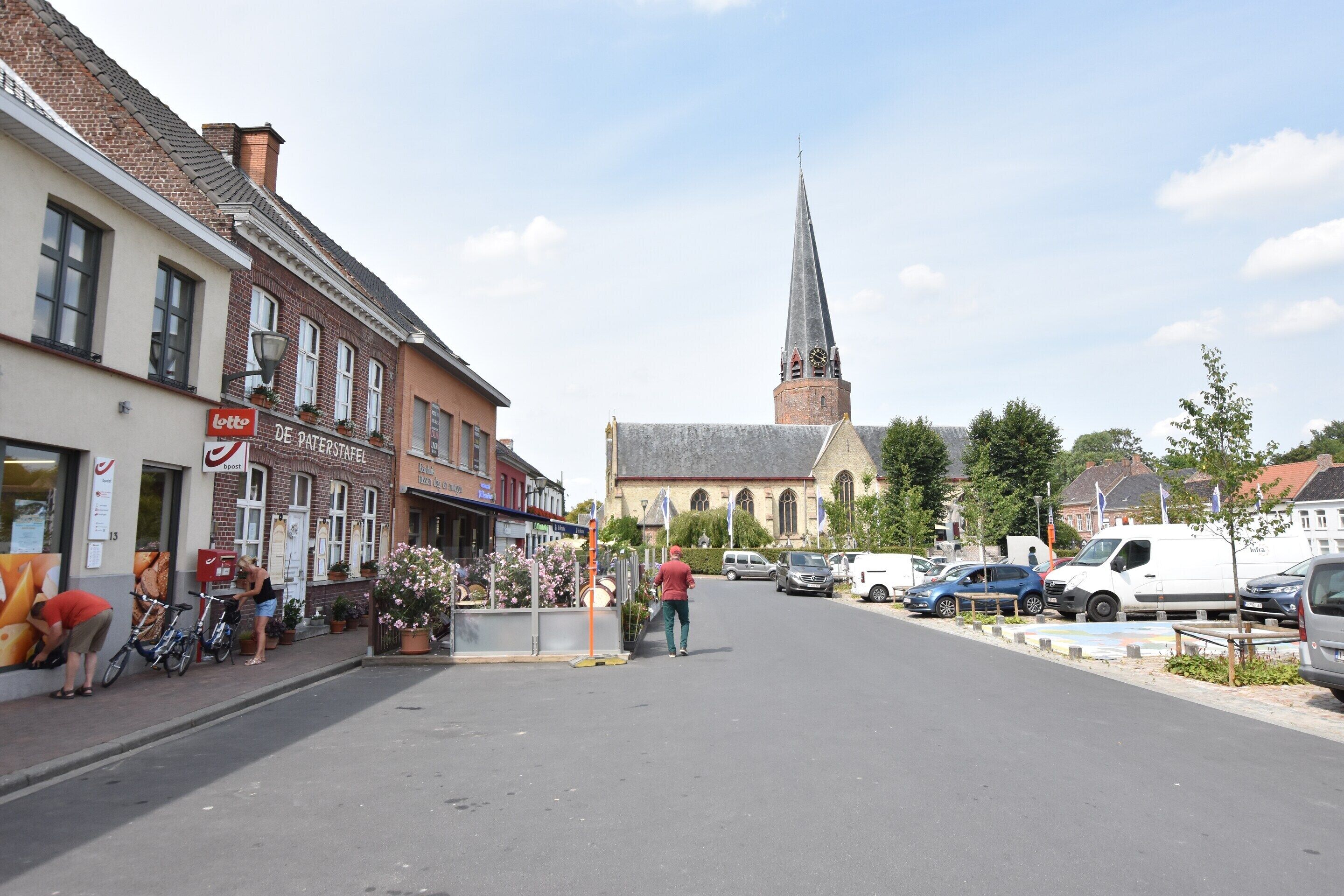 A street with buildings, a church, and parked cars.