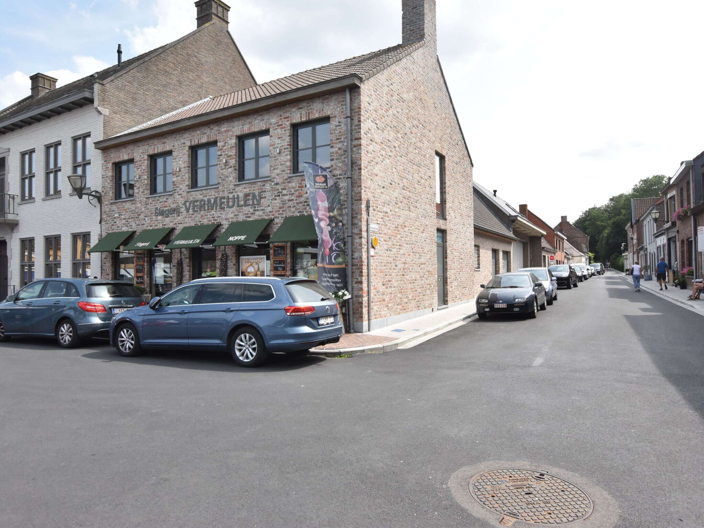 A street with parked cars and a building with a sign reading "VERMEULEN".