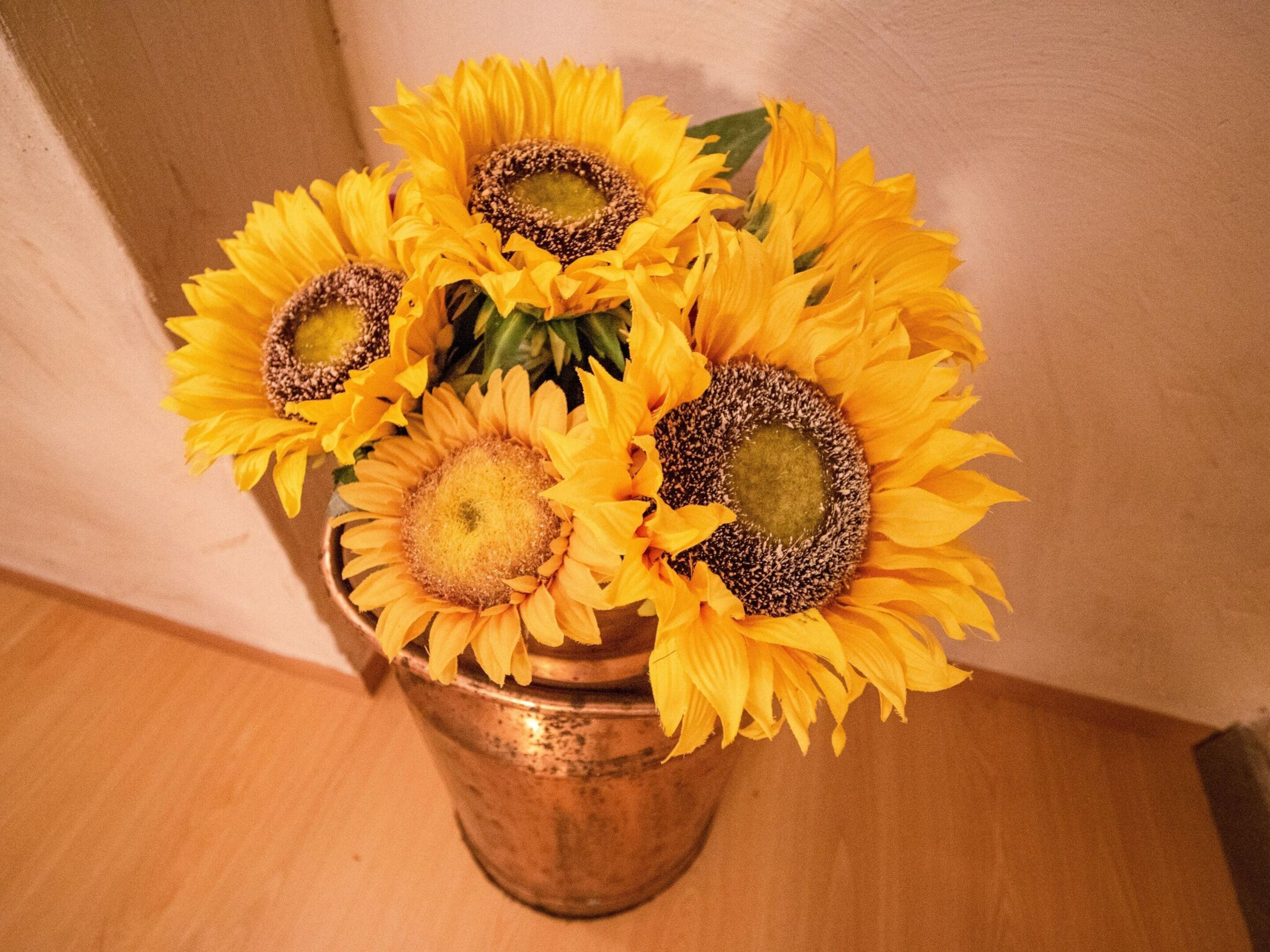 A copper vase with sunflowers on a wooden surface.
