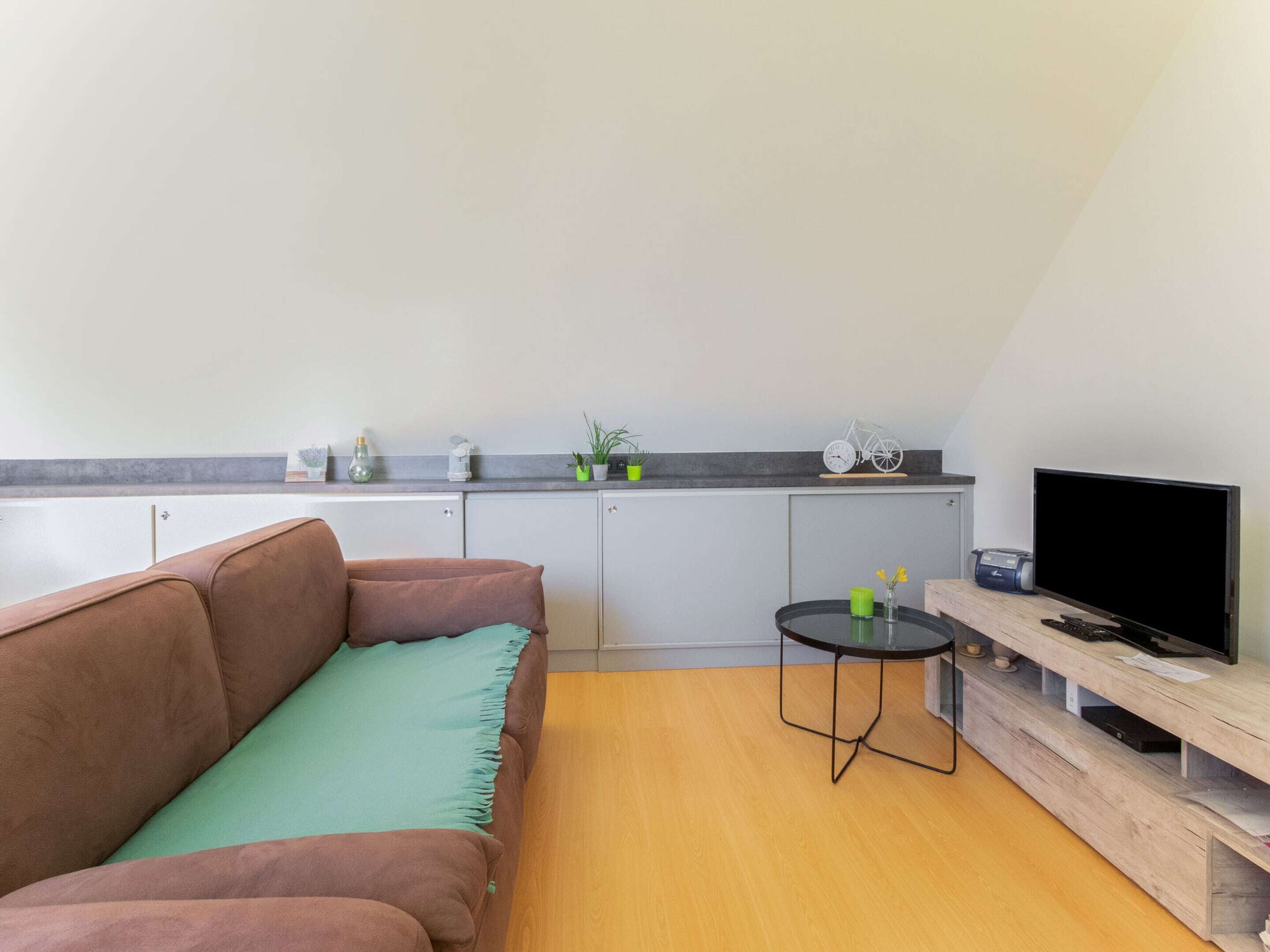 A compact living space with a sofa, a small round table, a TV, and a kitchenette area.