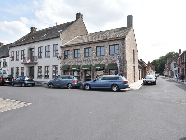 A street view with a building labeled 'VERMUGEN' featuring a brick facade and green awnings. - Apartment in Watou Near French Border (Poperinge)