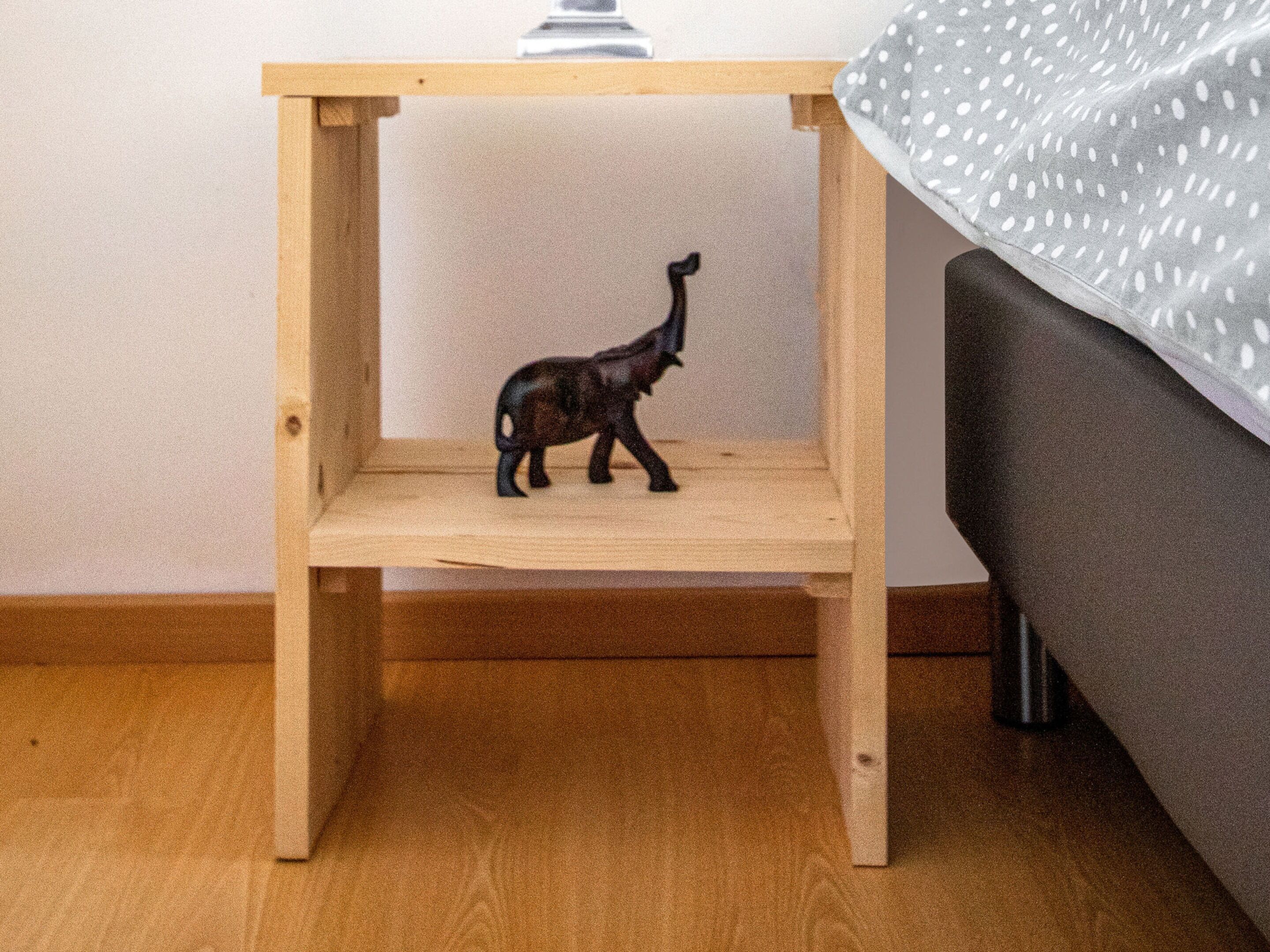 Ein kleines Holzregal mit einer Giraffenfigur darauf, platziert auf einem Holzboden neben einem grauen Sofa.