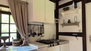 Cozinha com fogão, pia, utensílios pendurados e janela com cortinas.