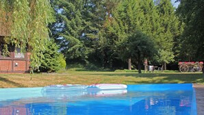Piscina com um deque flutuante, rodeada por árvores e um edifício de tijolos.